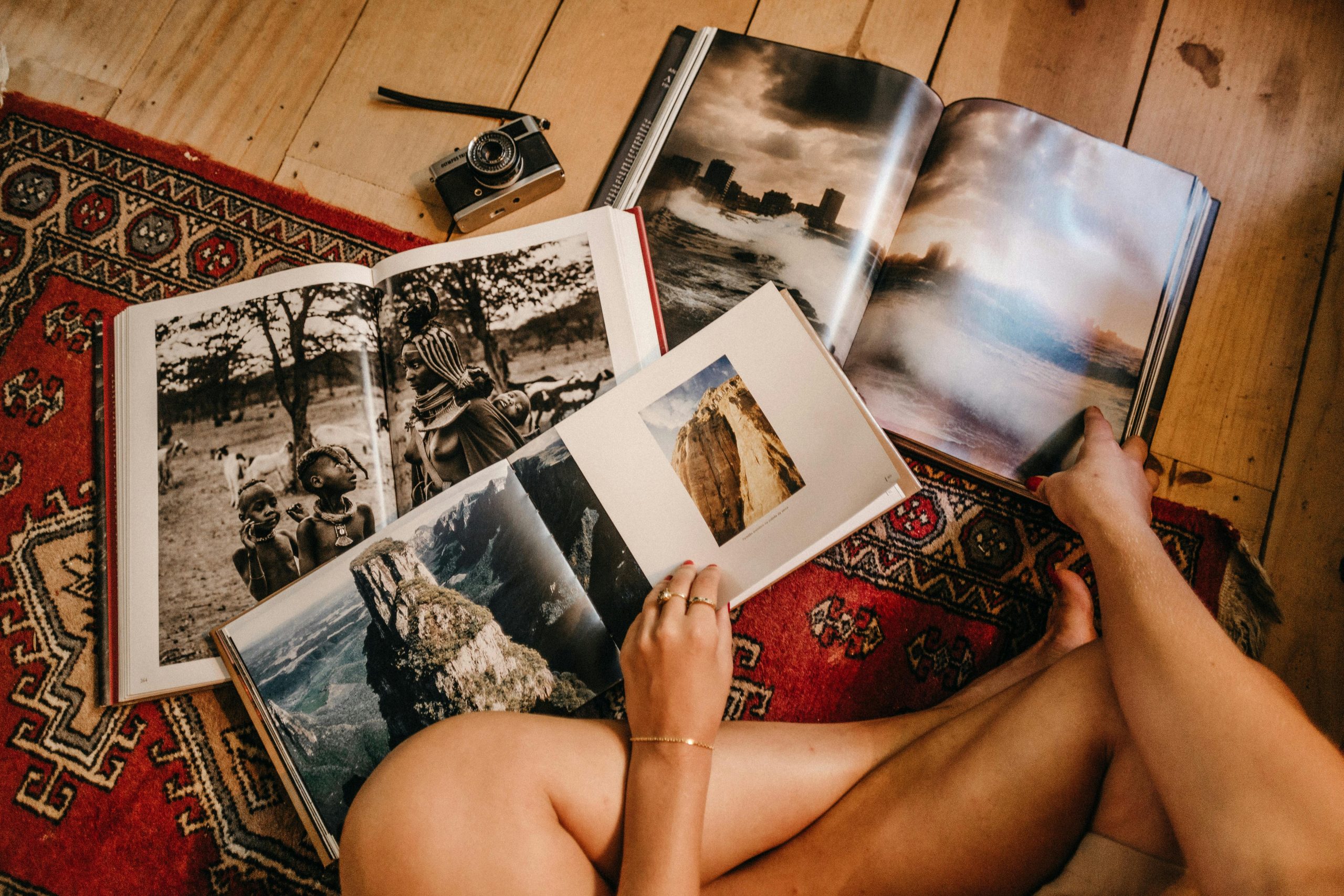 Home Person browsing photography books on a vintage rug with an analog camera in view.